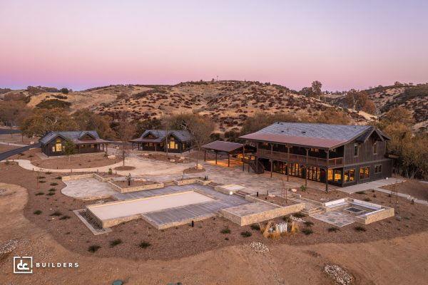 Aerial view of three homes, several large pools, and an outdoor dining area surrounded by desert mountains.